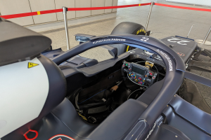 Das Cockpit eines Formel-E-Autos in einer Ausstellung, mit einem Lenkrad im Vordergrund und Polen mit Bändern um das Auto.