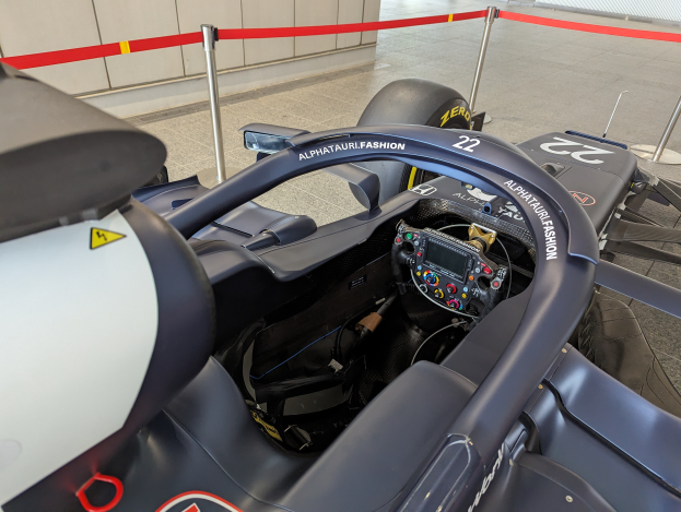 Das Cockpit eines Formel-E-Autos in einer Ausstellung, mit einem Lenkrad im Vordergrund und Polen mit Bändern um das Auto.