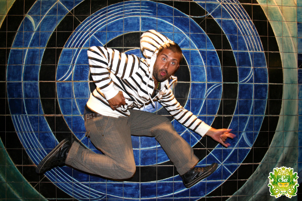 Ein Mann tanzt vor einem farbenfrohen Hintergrund mit einem Logo mit Text in der rechten oberen Ecke.