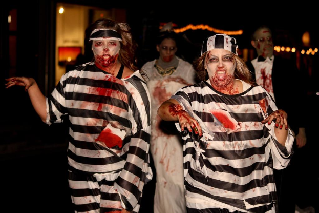 Zwei Frauen in Schwarz-Weiß-Kleidern mit Zombie-Make-up stehen im Vordergrund, dahinter ein Paar in anderer Schminke und Lichter im Hintergrund.