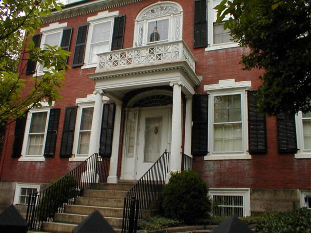 Ein Gebäude mit Glasfenstern und weißen Rändern, das eine Treppe mit schwarzen Gittern auf beiden Seiten hat, flankiert von Bäumen auf beiden Seiten.