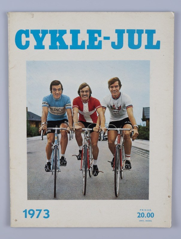 Drei Menschen auf Fahrrädern auf einer Straße mit Häusern, Bäumen und einem klaren blauen Himmel; "Cykle-Jul 1973 - Cyclocross Magazine" Text oben und unten.