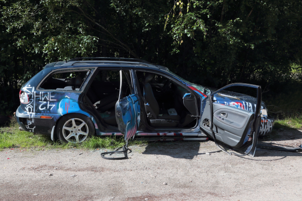 Auto auf der Seite der Straße gestürzt, umgeben von Gras und Bäumen.