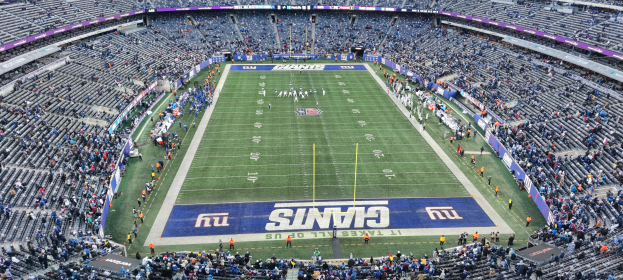 Ein Fußballstadion voller Zuschauer, Spieler und verschiedener Gegenstände auf dem Feld, einschließlich Tafeln mit Text und Reihen von Stühlen.