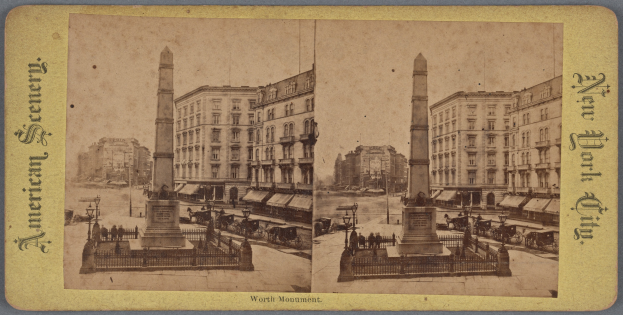 Altes Schwarz-Weiß-Foto einer Stadtstraße mit einem zentralen Denkmal umgeben von Gebäuden, Straßenmöbeln, parkenden und fahrenden Fahrzeugen, Fußgängern auf dem Gehweg und einem sichtbaren Himmel.