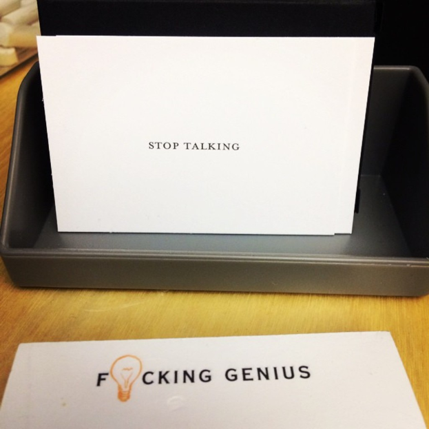 Ein Druckerbox mit einem Blatt Papier darauf, auf dem der Text "Hör auf zu reden" steht, und einem weiteren Blatt auf dem Tisch mit dem Text "Verdammter Genius".