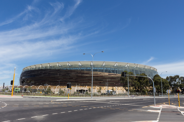 Ein großes Stadion mit starkem Verkehr davor, umgeben von verschiedenen Straßeninfrastrukturen, Geländern, Bäumen und einem bewölkten Himmel.