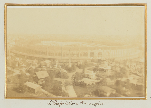 Altes Schwarz-Weiß-Foto eines Stadions, das zentral in einer Stadt gelegen ist, umgeben von Gebäuden, Bäumen und Strommasten, mit Text am unteren Rand.