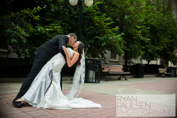 Ein Brautpaar küsst vor einer Kulisse aus Bänken, Mülltonnen und Bäumen.