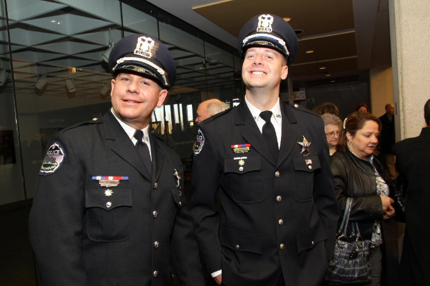 Zwei lachende Beamte im Vordergrund, mit Menschen in der Mitte, Glasfenstern links, Lampen und Decke oben und Säulen und Menschen rechts.