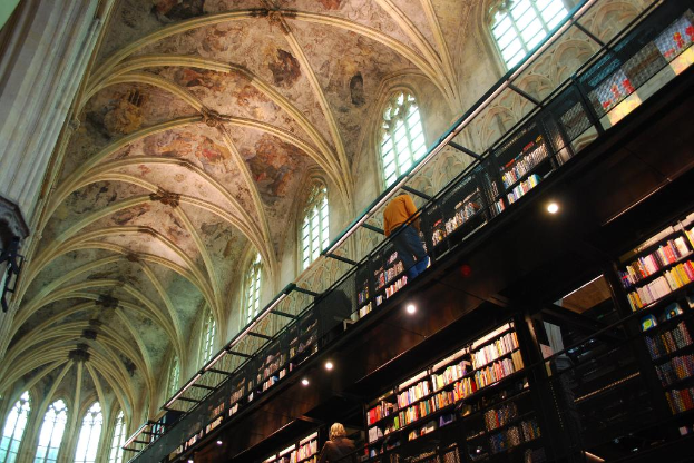 Das Innere eines Gebäudes mit mehreren Personen, beleuchteten Lampen und Büchern auf Regalen.