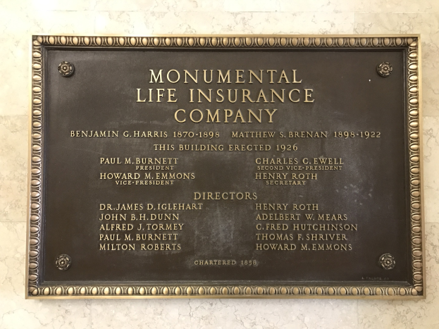 Plakette für Monumental Lebensversicherungsgesellschaft an einer Gebäudewand mit dunklem Material und dekorativem Rahmen.