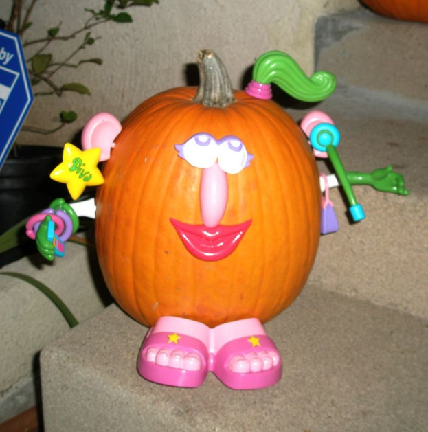 Ein Kürbis auf einer Treppe mit Spielzeugen darauf, eine Pflanze und ein blaues Objekt links und ein weiterer Kürbis oben.