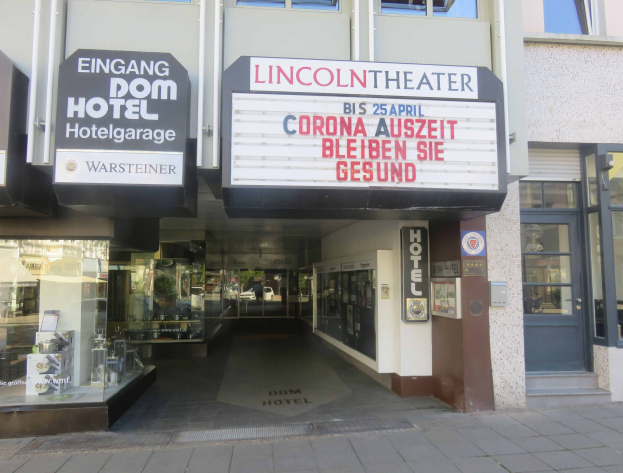 Außenansicht des Lincoln Theaters in Berlin, Deutschland, mit Glasfenstern und -türen sowie einer Tafel und einem Inneren mit verschiedenen Gegenständen, die eine belebte Stadtatmosphäre suggerieren.