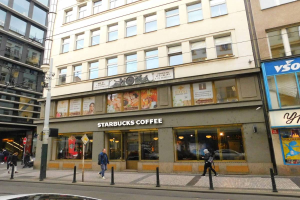 Ein Starbucks-Café an einer Straßenecke in Berlin, Deutschland, mit Menschen auf dem Gehweg, einem Auto auf der Straße und einem Mast mit Drähten an der Seite der Straße.