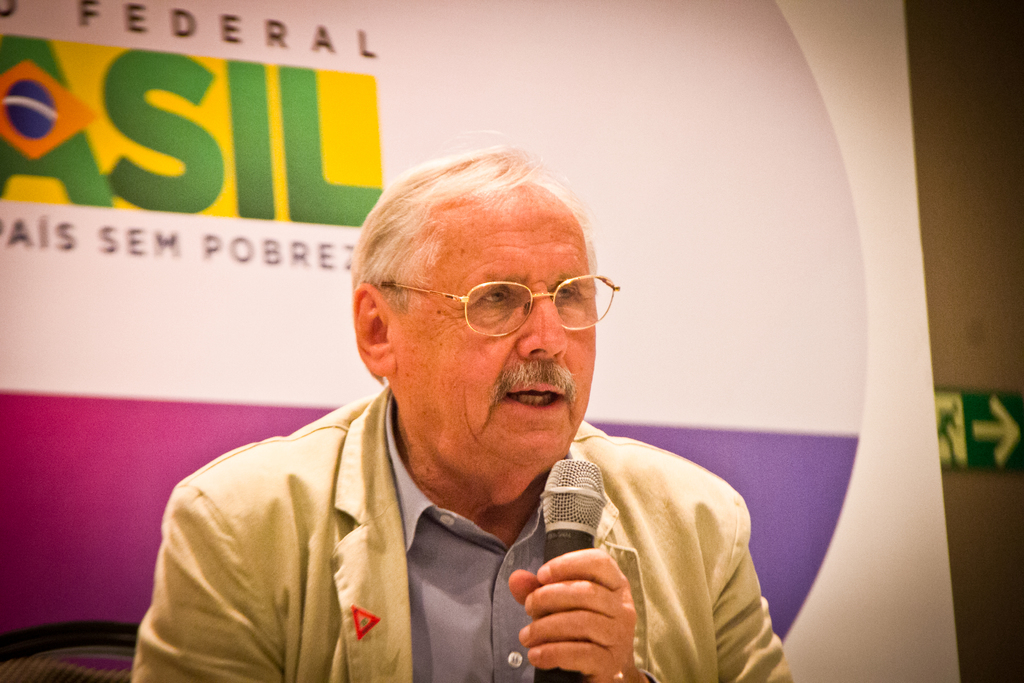 Eine Person, die in ein Mikrofon spricht und von einem Banner mit dem Wort 'Bundes' dahinter umgeben ist.