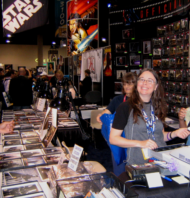 Eine Frau posiert an einem Verkaufstresen in einem mit Bildern, Büchern und Plakaten gefüllten Geschäft, während Kunden stöbern und einkaufen.