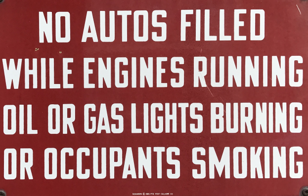 Ein rotes Schild mit weißer Schrift, das davor warnt, Autos während des Laufens des Motors, des Brennens von Öl oder Gas oder des Rauchens von Insassen aufzufüllen.