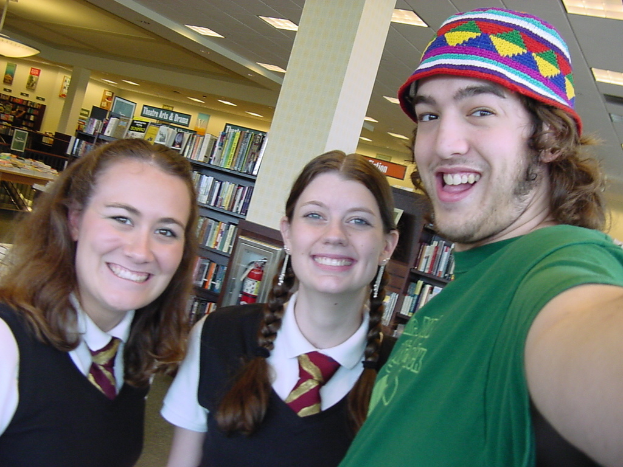 Ein Mann und zwei Schüler machen ein Selfie in einer Bibliothek, mit Bücherregalen voller Bücher im Hintergrund.