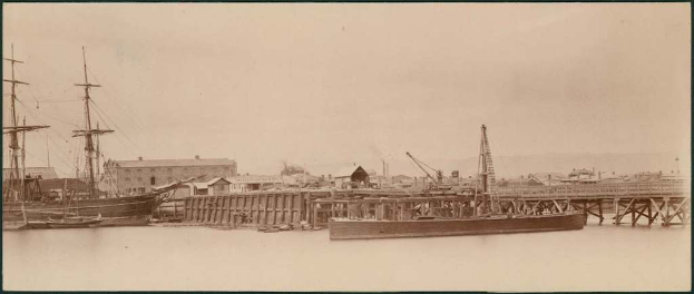 Ein Gewässer mit Booten, Gebäuden und Strommasten am Ufer unter einem Himmel.