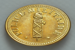 Eine Goldm├╝nze mit der Aufschrift "Police Militaire" vor einem weißen Hintergrund.