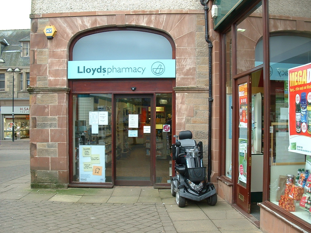 Eine Apotheke mit einem Fahrzeug davor und einem Gebäude in der linken Ecke.