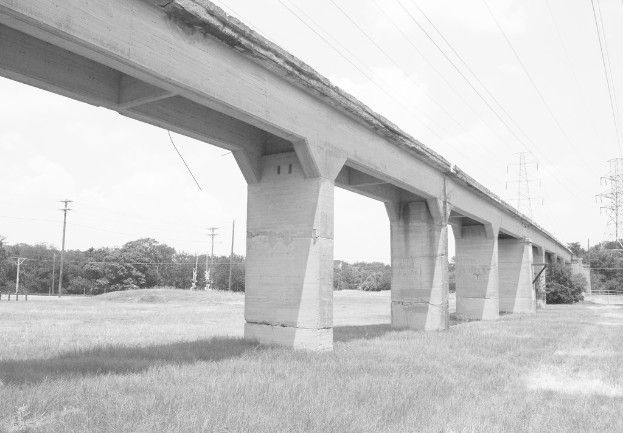 Eine Betonbrücke auf einer grünen Wiese mit einem großen elektrischen Mast und Kabeln darüber und mehreren Bäumen und elektrischen Masten im Hintergrund.