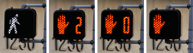 Eine Ampel mit drei Signalen an einem Gebäude angebracht, mit einer Wand im Hintergrund.