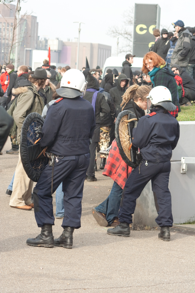 Eine Gruppe von Menschen, die auf einer Straße gehen, mit zwei Personen in der Front, die wie Polizisten aussehen, Gebäuden im Hintergrund und Erde unten.