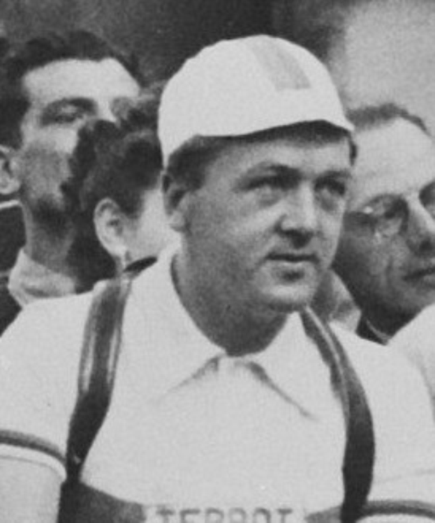 Ein Schwarz-Weiß-Foto eines Mannes in einer Mütze und Hosenträgern, der vor einer Gruppe von Menschen steht, die mutmaßlich ein legendärer Fußballspieler ist.