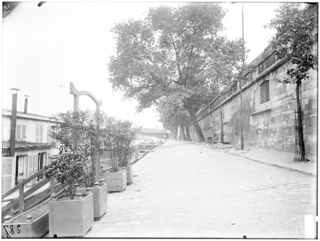 Eine schwarz-weiße Straßenansicht des New Yorker Staatsgefängnisses mit einer Wand auf der rechten Seite, Bäumen auf der linken Seite und einer Brücke im Hintergrund, beschriftet mit "New York City, New York, New Jersey, NY, USA, USA".