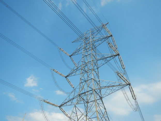Eine Hochspannungsleitung am blauen Himmel mit Wolken, die sich von einem Turm am unteren Bildrand erstreckt.