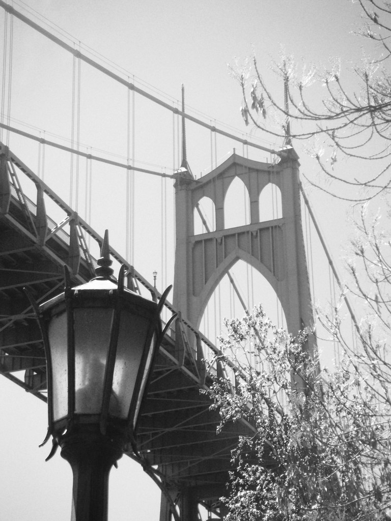 Ein altes Bild einer Hängebrücke mit einem schwarzen Laternenmast vorne unten und einem Baum in der rechten Ecke.
