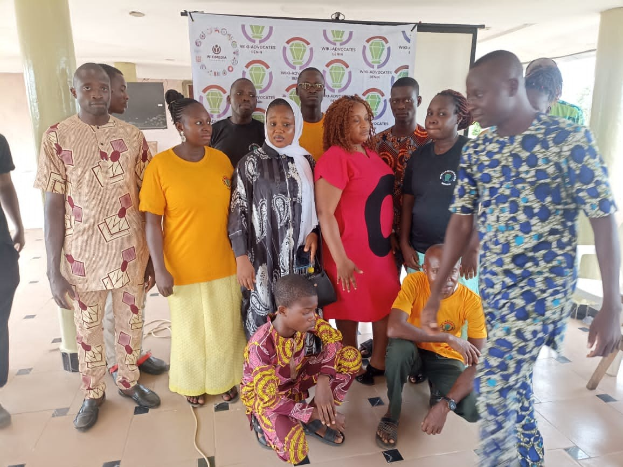 Eine Gruppe von Menschen vor einem Banner mit der Aufschrift "Advocates in Ghana: Ein Schritt-f├╝r-Schritt-F├╝hrer", umgeben von St├╝hlen, S├Ąulen, einem Fernseher und einer Decke mit Deckenleuchten.