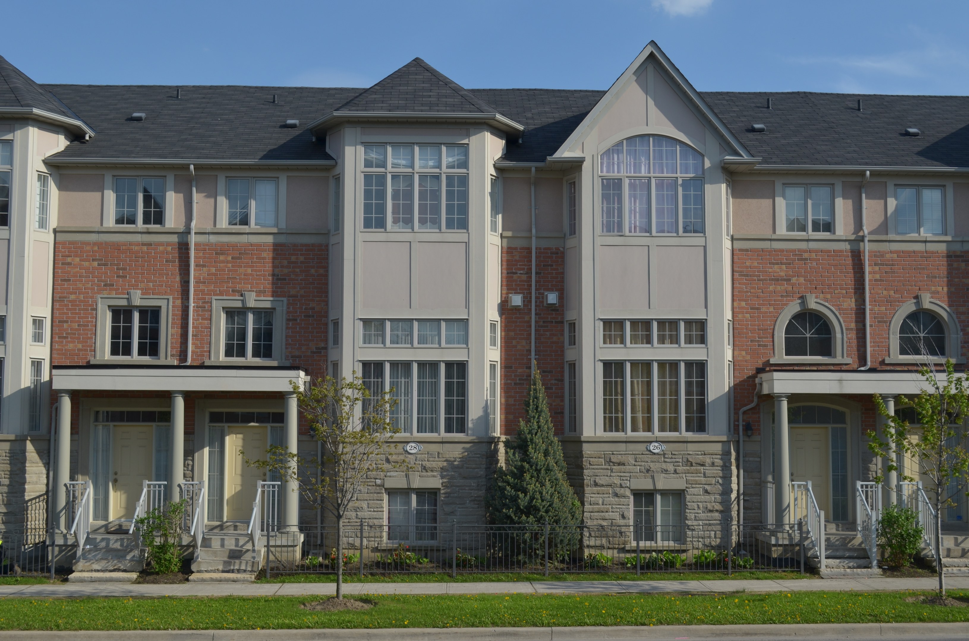 Eine Reihe von Stadthäusern in einer Wohngegend mit Fenstern, Türen, Säulen, Geländern, Stufen, Pflanzen, Bäumen, Gras und Himmel.