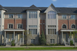 Eine Reihe von Stadthäusern in einer Wohngegend mit Fenstern, Türen, Säulen, Geländern, Stufen, Pflanzen, Bäumen, Gras und Himmel.