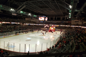 Eishockeyspiel in einer großen Arena mit Zuschauern, eine von einem Zaun umgebene Eisfläche, Banner, Deckenbeleuchtung und zwei Bildschirme; die Location ist die Columbus Blue Jackets Arena.