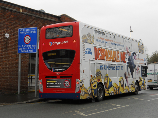 Ein weißer und roter Bus parkt auf einer Straße mit einer roten Backsteinwand und einem blauen Warnschild im Hintergrund.