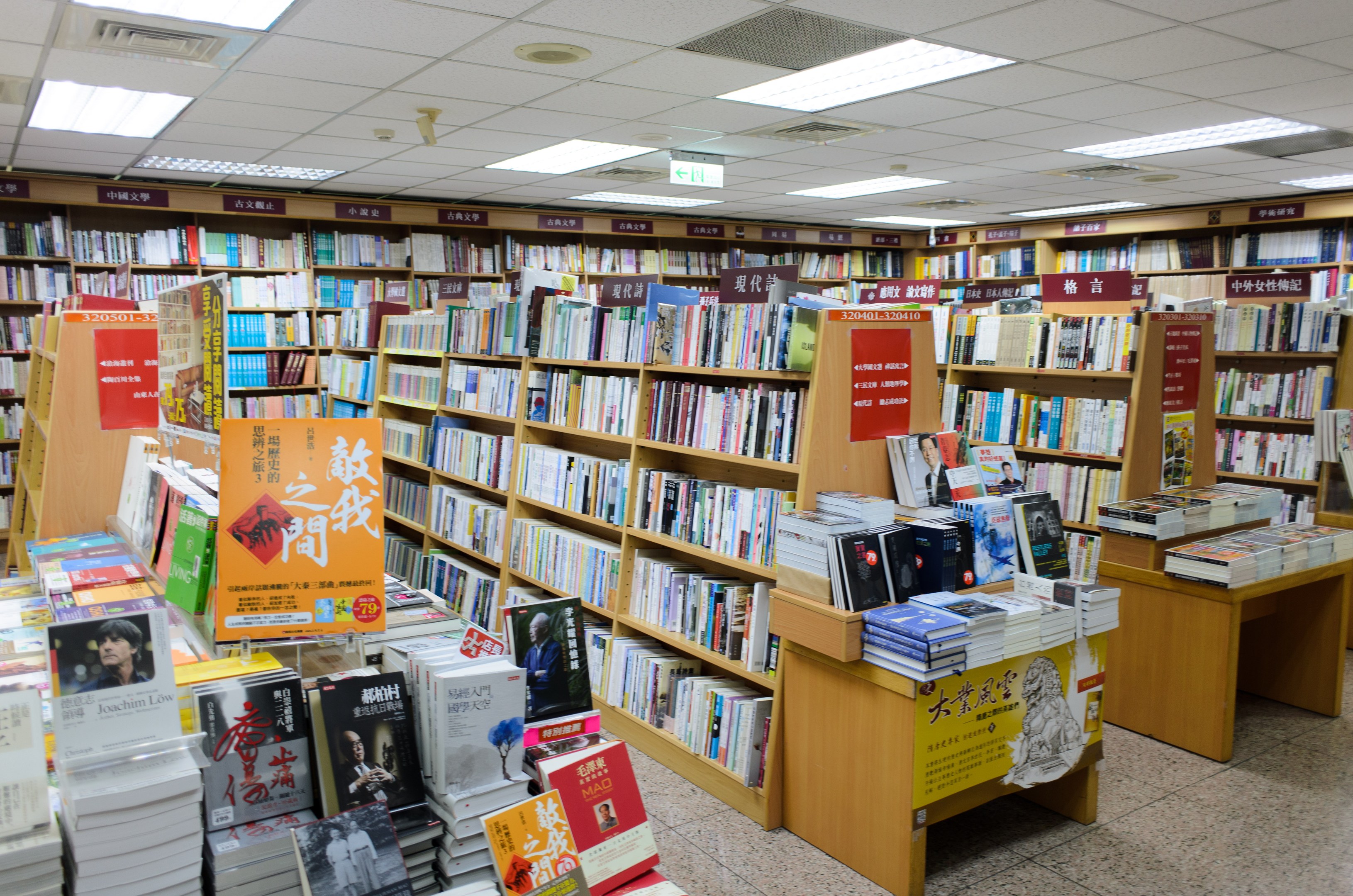 Ein gut organisierter Buchladen mit ordentlich aufgestellten Büchern auf Regalen und Tischen, mit informativen Schildern auf dem Boden und Deckenlampen.