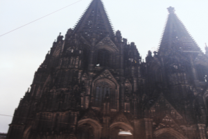 Der Kölner Dom in Köln, Deutschland, mit seinen Spitzen, die in den Himmel ragen, und ein paar Menschen vor dem Gebäude mit sichtbaren Kabeln im Hintergrund.