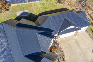 Ein Haus mit Solarpaneelen auf dem Dach, umgeben von Bäumen, Gras und einem Zaun, von oben betrachtet.