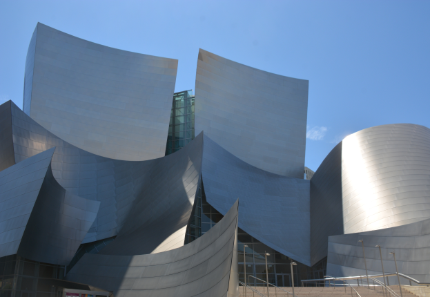 Das Künstler-Konzertgebäude in Los Angeles, ein modernes Gebäude mit Glaswänden und Treppen mit Geländern, die zum Eingang führen, umgeben von Laternenmasten, mit einer Tafel mit Text im Vordergrund und einem bewölkten Himmel im Hintergrund.