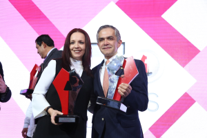 Zwei Menschen, die auf einer Bühne lächeln und Trophäen halten.