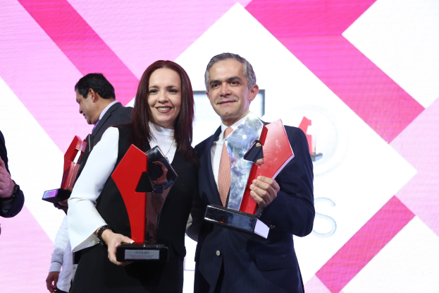 Zwei Menschen, die auf einer Bühne lächeln und Trophäen halten.