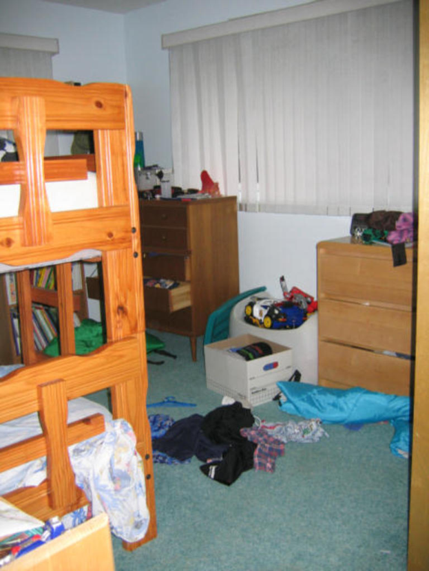 Ein Zimmer mit einem Stockbett, Schreibtisch, Tisch und diversen Gegenständen auf dem Boden.