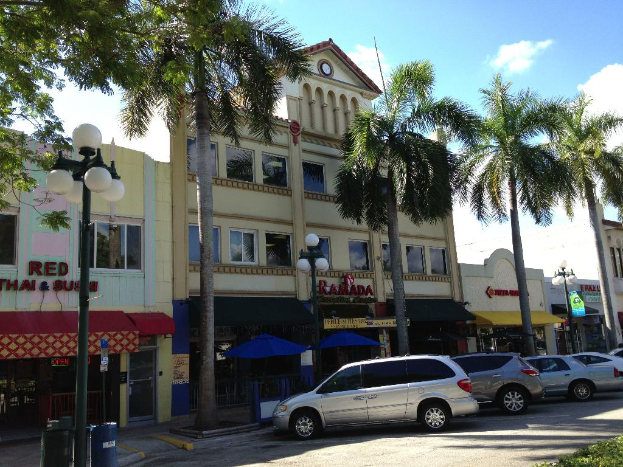 Einige Gebäude und Bäume mit mehreren Straßenlaternen und parkenden Autos.