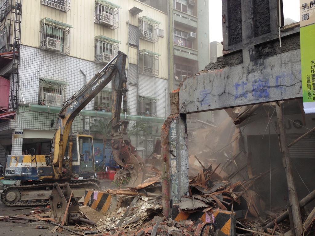 Ein Bagger auf einer Straße mit Schildern, Gebäuden mit Fenstern und dem Himmel im Hintergrund.