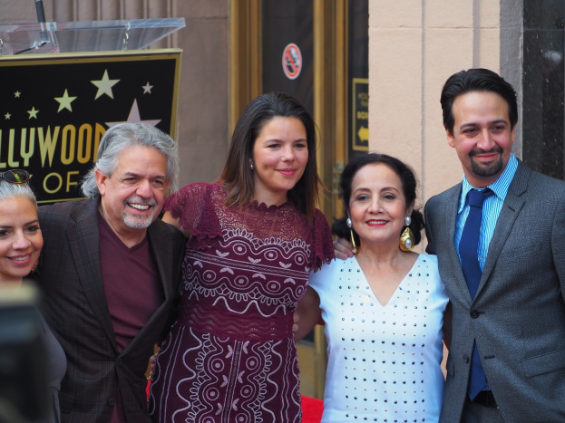 Gruppe von Menschen auf einem roten Teppich bei der Zeremonie auf dem Hollywood Walk of Fame posierend, mit einer Kamera links, einer Tafel mit Text, einem Glaspodest und einer Wand im Hintergrund.