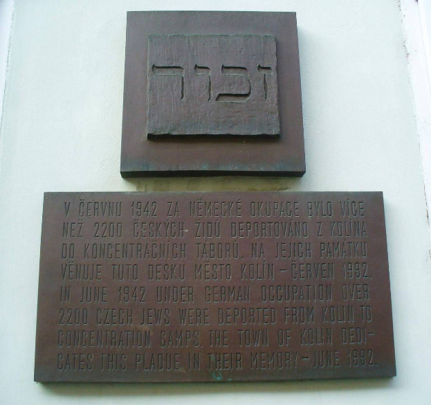 Metallplatte an einer Gebäudewand mit hebräischer Schrift, wahrscheinlich ein Denkmal für die jüdische Gemeinde.