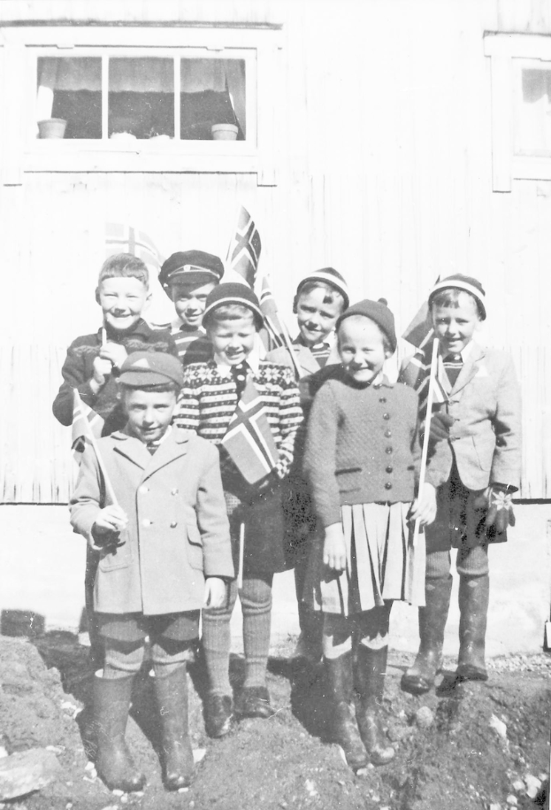 Eine Gruppe strahlender Kinder in Schwarz-Weiß, die Fahnen halten, steht vor einem Gebäude mit einer Wand und einem Fenster, wahrscheinlich eine schwedische Schule.